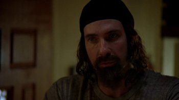 Movie still from “Wonderland” (2003), directed by James Cox – A man with long hair and a beard wearing a black hat; Close Up shot, Over the shoulder angle