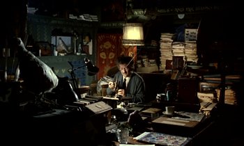 Movie still from “Wonderwall” (1968), directed by Joe Massot – A man sitting at a desk in front of a laptop computer; Wide shot, High angle