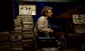 Movie still from “Wonderwall” (1968), directed by Joe Massot – A man standing in front of a pile of papers; Medium shot, Overhead angle