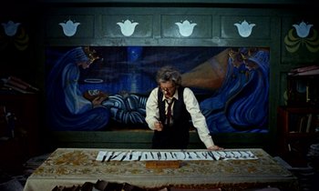 Movie still from “Wonderwall” (1968), directed by Joe Massot – An older man is playing a piano in front of a mural; Wide shot, Overhead angle