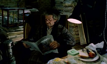 Movie still from “Wonderwall” (1968), directed by Joe Massot – An older man sitting in a chair while reading a newspaper; Medium shot, High angle