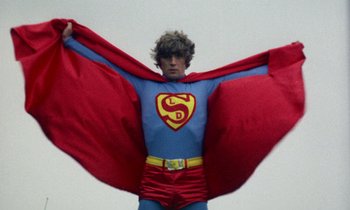 Movie still from “Wonderwall” (1968), directed by Joe Massot – A man dressed as a superman with a cape; Medium shot, Low angle