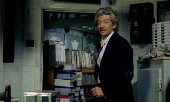 Movie still from “Wonderwall” (1968), directed by Joe Massot – A man standing in front of a shelf of books; Medium shot, Over the shoulder angle