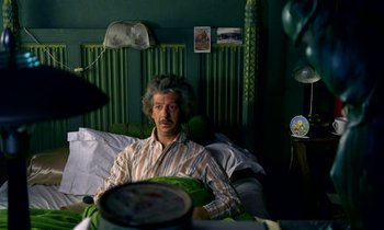 Movie still from “Wonderwall” (1968), directed by Joe Massot – A man sitting on a couch in a living room; Medium shot, High angle