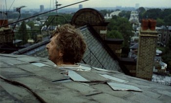 Movie still from “Wonderwall” (1968), directed by Joe Massot – A man sitting on top of a roof looking out over a city; Medium shot, High angle