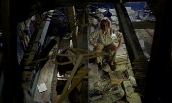 Movie still from “Wonderwall” (1968), directed by Joe Massot – A man standing inside of a room with a pile of rubble; Wide shot, Overhead angle