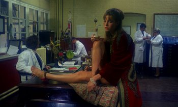 Movie still from “Wonderwall” (1968), directed by Joe Massot – A woman sitting on top of a table holding a wine glass; Wide shot, High angle
