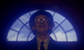 Movie still from “Wonderwall” (1968), directed by Joe Massot – A man wearing a hat and glasses in front of a stained glass window; Close Up shot, Low angle
