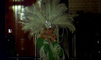 Movie still from “Wonderwall” (1968), directed by Joe Massot – A woman in a green dress wearing a white feathered headdress; Close Up shot, Low angle