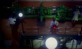 Movie still from “Wonderwall” (1968), directed by Joe Massot – A man sitting on a chair in a room with green walls; Extreme Wide shot, Overhead angle