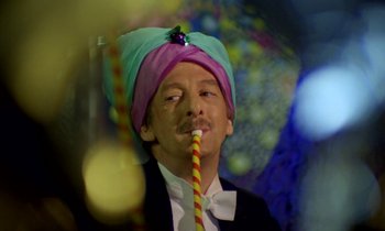 Movie still from “Wonderwall” (1968), directed by Joe Massot – A man in a bow tie wearing a hat and holding a straw; Close Up shot, Low angle