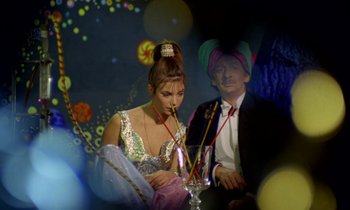 Movie still from “Wonderwall” (1968), directed by Joe Massot – A man and a woman sitting at a table with drinks; Medium shot, Low angle