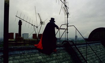 Movie still from “Wonderwall” (1968), directed by Joe Massot – A man in a top hat and a long black cape on the roof of a building; Wide shot, Low angle