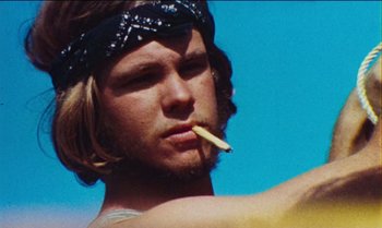 Movie still from “Woodstock” (1970), directed by Michael Wadleigh – A man with a bandana on his head smoking a cigarette in front of a blue sky; Close Up shot, Low angle