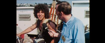 Movie still from “Woodstock” (1970), directed by Michael Wadleigh – A man is being interviewed by an older man; Medium shot, Over the shoulder angle
