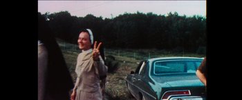 Movie still from “Woodstock” (1970), directed by Michael Wadleigh – An old photo of a woman giving the peace sign; Medium shot, Low angle