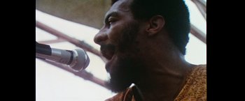 Movie still from “Woodstock” (1970), directed by Michael Wadleigh – A man with a beard is singing into a microphone; Extreme Close Up shot, Low angle