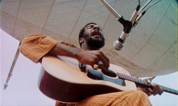 Movie still from “Woodstock” (1970), directed by Michael Wadleigh – A man holding a guitar in front of a microphone; Close Up shot, Low angle