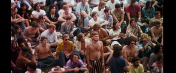 Movie still from “Woodstock” (1970), directed by Michael Wadleigh – A crowd of people sitting on the ground watching a performance; Wide shot, High angle
