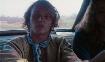 Movie still from “Woodstock” (1970), directed by Michael Wadleigh – A man with long hair sitting in the back of a car; Close Up shot, Low angle
