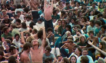 Movie still from “Woodstock” (1970), directed by Michael Wadleigh – A crowd of people sitting and standing in a stadium; Wide shot, High angle