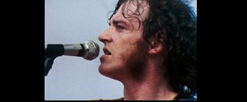 Movie still from “Woodstock” (1970), directed by Michael Wadleigh – A person singing into a microphone; Close Up shot, Low angle