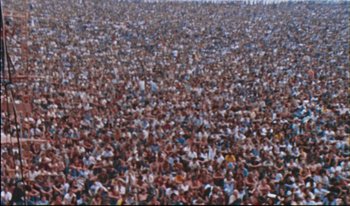 Movie still from “Woodstock” (1970), directed by Michael Wadleigh – A large crowd of people sitting in a field; Extreme Wide shot, High angle