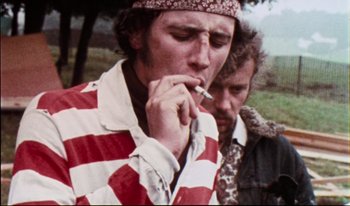 Movie still from “Woodstock” (1970), directed by Michael Wadleigh – A man smoking a cigarette next to another man; Close Up shot, Low angle