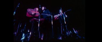 Movie still from “Woodstock” (1970), directed by Michael Wadleigh – A group of people playing guitars on a stage; Wide shot, High angle