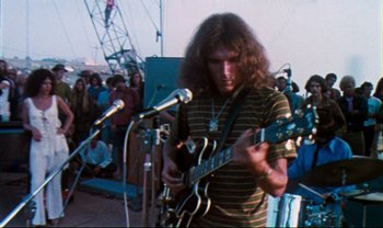 Movie still from “Woodstock” (1970), directed by Michael Wadleigh – A man playing a guitar in front of a crowd; Medium shot, Low angle