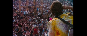 Movie still from “Woodstock” (1970), directed by Michael Wadleigh – A crowd of people are gathered around a microphone; Wide shot, High angle