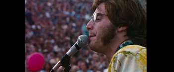 Movie still from “Woodstock” (1970), directed by Michael Wadleigh – A man is speaking into a microphone in front of a crowd; Close Up shot, Low angle