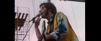 Movie still from “Woodstock” (1970), directed by Michael Wadleigh – A man is singing into a microphone on a stage; Medium shot, Low angle