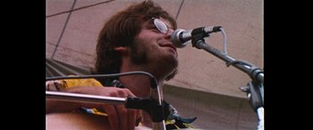 Movie still from “Woodstock” (1970), directed by Michael Wadleigh – A man with a guitar and a microphone on a stage; Close Up shot, Low angle