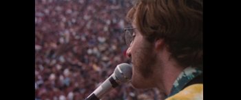 Movie still from “Woodstock” (1970), directed by Michael Wadleigh – A man with glasses is speaking into a microphone; Close Up shot, High angle