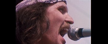 Movie still from “Woodstock” (1970), directed by Michael Wadleigh – A person singing with a microphone; Close Up shot, Low angle
