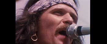Movie still from “Woodstock” (1970), directed by Michael Wadleigh – A person singing on a microphone; Close Up shot, Low angle