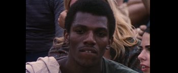 Movie still from “Woodstock” (1970), directed by Michael Wadleigh – A man's face in front of a group of people; Close Up shot, Low angle