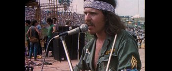 Movie still from “Woodstock” (1970), directed by Michael Wadleigh – A man with long brown hair is singing into a microphone; Close Up shot, Low angle