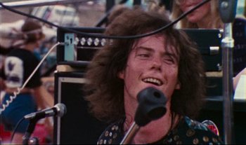 Movie still from “Woodstock” (1970), directed by Michael Wadleigh – A man with long hair is singing into a microphone; Close Up shot, Low angle