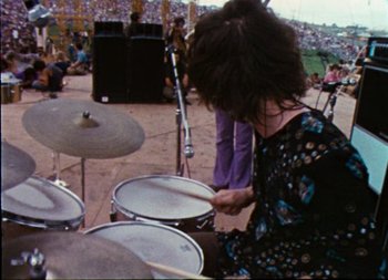 Movie still from “Woodstock” (1970), directed by Michael Wadleigh – A person playing drums in front of an audience; Medium shot, High angle