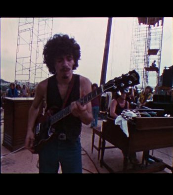 Movie still from “Woodstock” (1970), directed by Michael Wadleigh – A man playing a guitar in front of a crowd; Medium shot, High angle