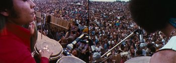 Movie still from “Woodstock” (1970), directed by Michael Wadleigh – A large crowd of people sitting in front of a microphone; Extreme Wide shot, High angle