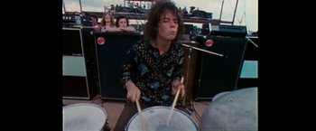 Movie still from “Woodstock” (1970), directed by Michael Wadleigh – A man playing drums in front of a group of onlookers; Medium shot, Low angle