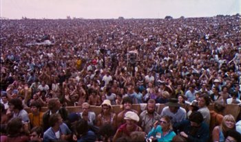 Movie still from “Woodstock” (1970), directed by Michael Wadleigh – A large crowd of people sitting in a stadium; Extreme Wide shot, High angle
