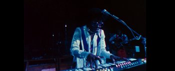 Movie still from “Woodstock” (1970), directed by Michael Wadleigh – A man playing a keyboard in front of a microphone; Medium shot, Low angle