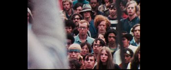 Movie still from “Woodstock” (1970), directed by Michael Wadleigh – A large group of people gathered together in a crowd; Medium shot, High angle