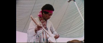 Movie still from “Woodstock” (1970), directed by Michael Wadleigh – A man playing a guitar while wearing a bandanna; Medium shot, Low angle