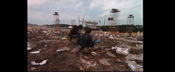Movie still from “Woodstock” (1970), directed by Michael Wadleigh – Two people sitting on a pile of rubble in a field; Wide shot, High angle