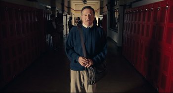 An older man standing in a hallway holding a bag